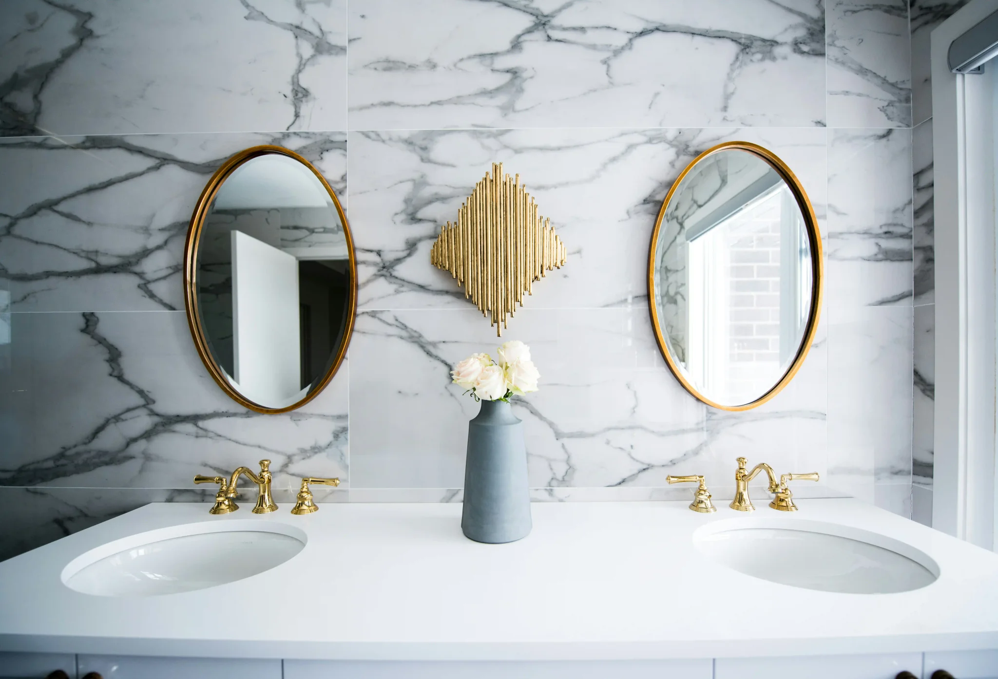 Luxury bathroom with large white marble tile walls, dual sinks, and gold faucet fixtures