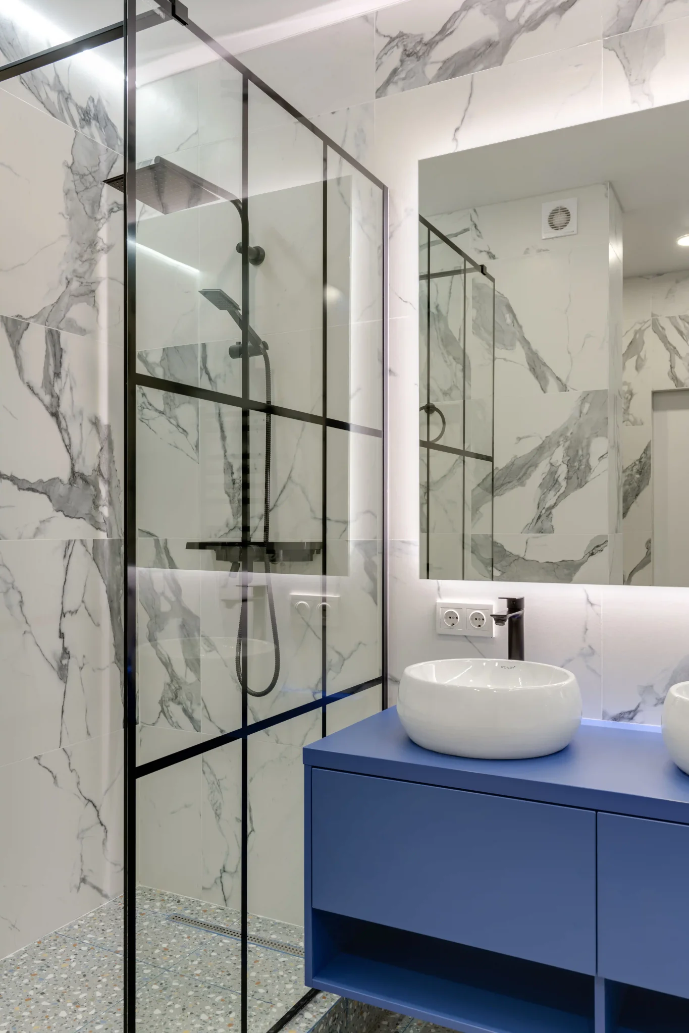 Modern bathroom with white marble porcelain tile, black framed glass shower, and blue vanity
