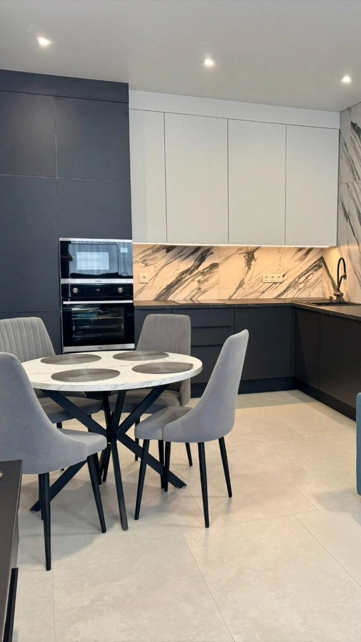 Modern kitchen with dramatic marble slab backsplash, dark lower cabinets, and white upper cabinets