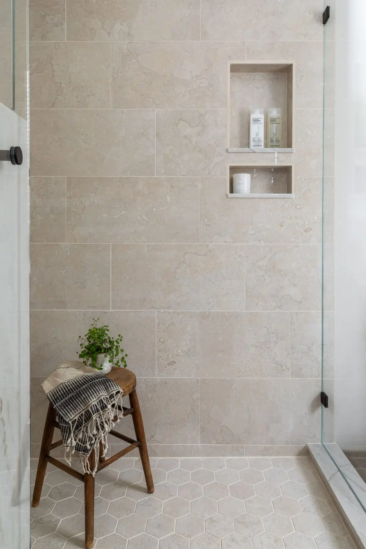 Shower with large-format travertine-look wall tile, hexagon mosaic floor, and built-in niche
